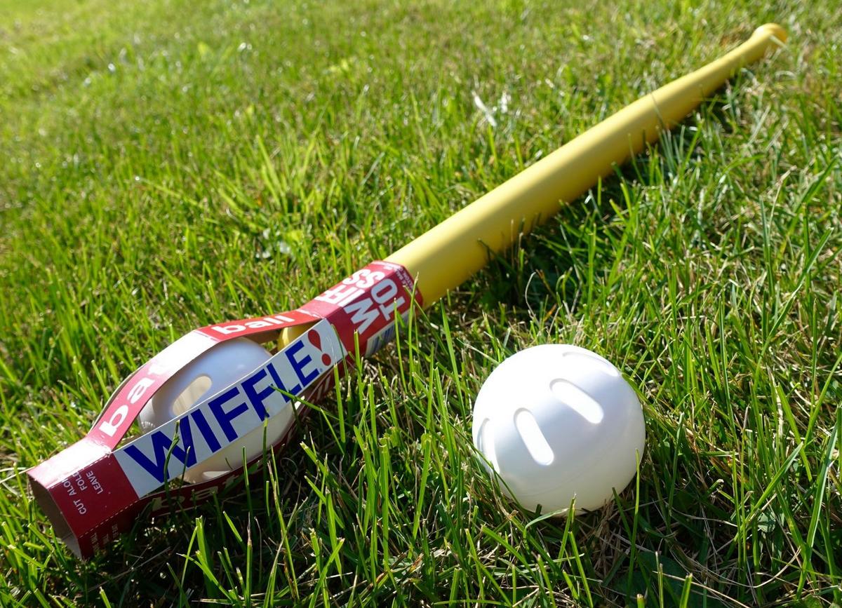 A yellow Wiffle bat and white Wiffle ball lying in green grass